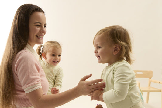 Smiling mother kneeling and holding hands with a baby taking steps in a FJÖRA MOVE onesie